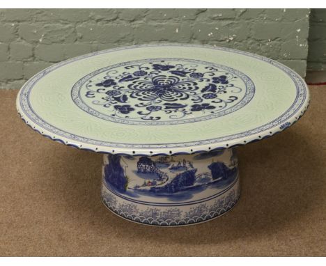 A circular ceramic coffee table decorated with blue and white floral design and Chinese scenes to the base.