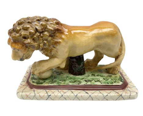 19th century Staffordshire style figure of a lion, modelled with paw resting upon globe, upon a naturalistically modelled rec