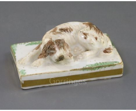 A Rockingham porcelain figure of a recumbent cocker spaniel, c.1830, on a rectangular green patch base with gilt edge, incise