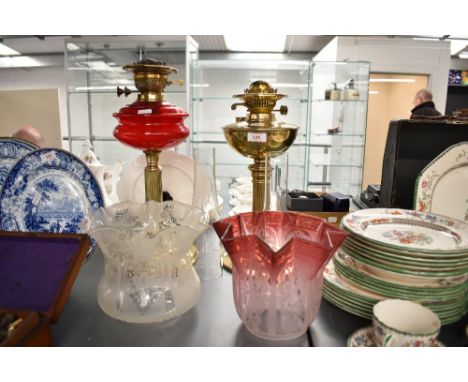 An early 20th century brass and ruby red glass oil lamp, h44, sold together with another brass oil lamp, two clear glass chim