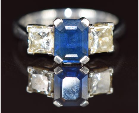 A platinum ring set with an emerald cut sapphire of approximately 2ct flanked by princess cut diamonds, each approximately 0.