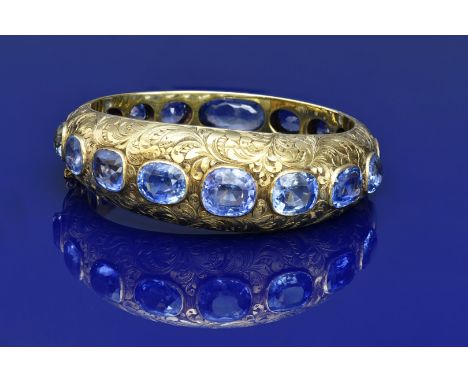 A c1900 18ct gold bangle with engraved floral decoration, set with seventeen natural cushion cut Ceylon Sapphires, the total 