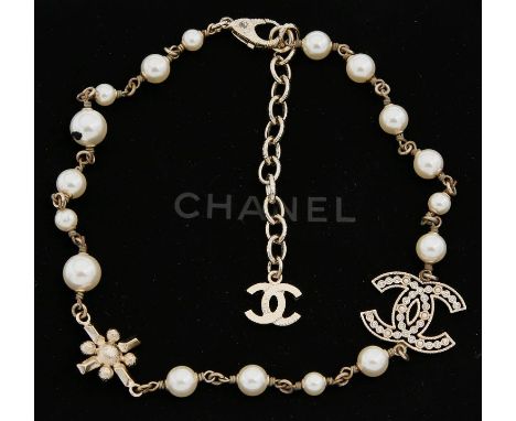 Kette, Chanel. Cremefarbene Kunstperlen, einzeln geknotet, D. ca. 0,6 bis 1 cm, dazwischen CC-Anhänger, besetzt mit Strassste