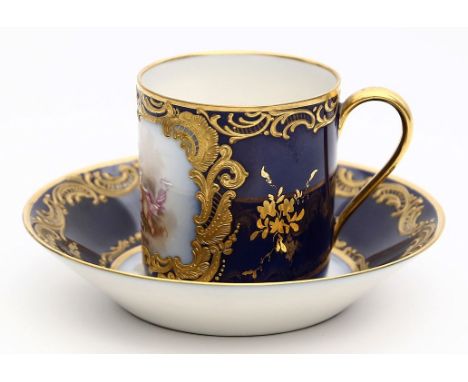 Prunktasse und Untertasse im Sèvres-Stil. Kobaltblauer Fond, teils mit reliefierten Rocaillen in Gold. Schauseite der Tasse u