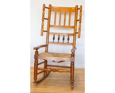 A 19th century Lancashire fruitwood winged rocking chair, having spindle back with rush seat, raised on ring turned supports.