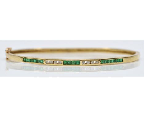 A 14K gold emerald &amp; diamond hinged bangle, channel set with brilliant cut diamonds and square cut emeralds, 60 x 50mm in