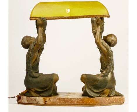 A French Art Deco cold painted table lamp, two ladies holding a green glass canopy above, raised on a brown variegated marble