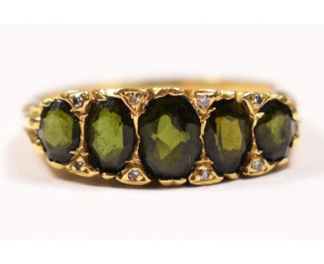 An 18ct gold five stone green tourmaline ring, carved claw set with mixed cut stones, diamond points between, T 1/2, 6.1gm. I