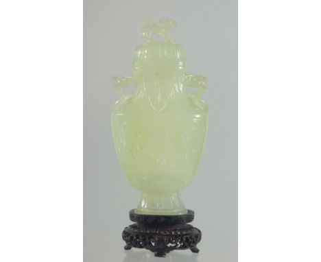 A CHINESE CARVED JADE LIDDED VASE AND WOODEN STAND, the vase with foo dog finial and drop ring handles, 17.5cm high (on stand