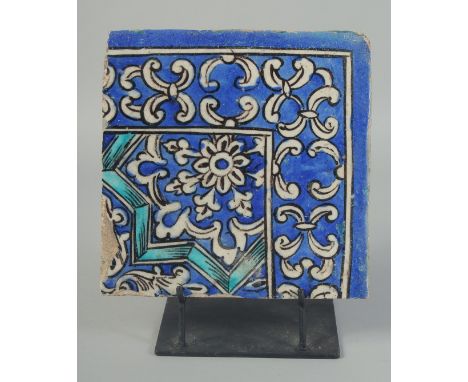 A PERSIAN QAJAR GLAZED POTTERY CORNER TILE, on a fitted metal stand, the tile painted with foliate decoration, tile measuring