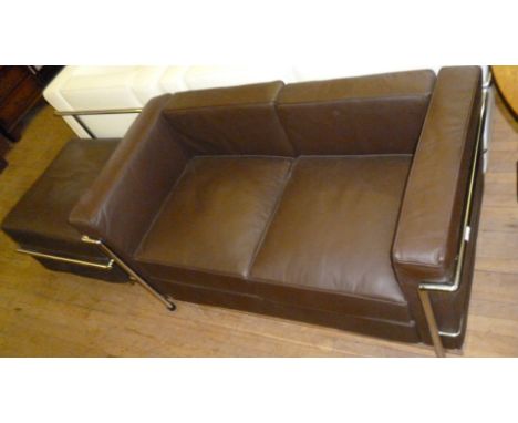 A Le Corbusier Petite Comfort two seater sofa, upholstered in a brown leather material with matching pouffe.