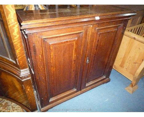 An early 20th c. dark Oak floor-standing Cupboard having a pair of raised and fielded panelled doors having Mahogany cross-ba