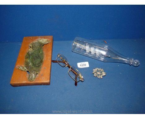 A wooden plaque decorated with brass parrot insert, glass ship in a bottle, pair of spectacles, etc.   