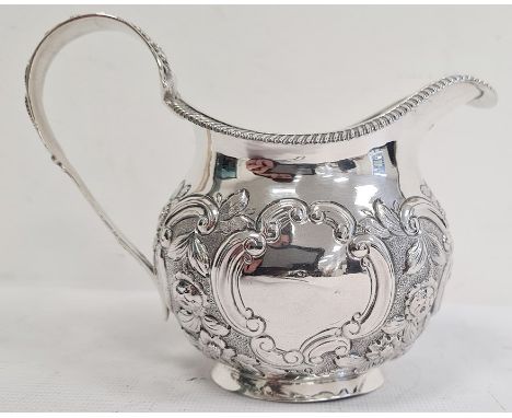 George IV silver milk jug, having gadrooned everted rim, ornate floral cornucopia decorated handle, the body repousse with ba