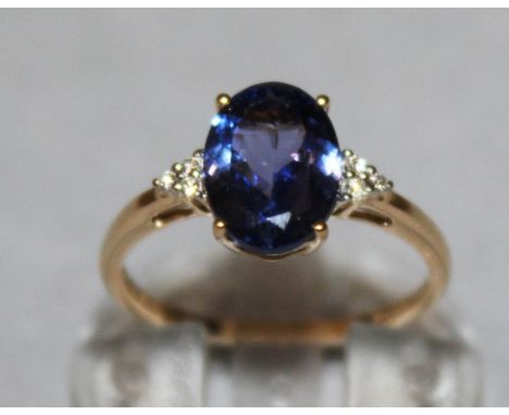 A TANZANITE OVAL RING with zircon shoulders, set in 9ct yellow gold.