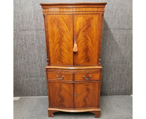 A mahogany veneered cabinet with pull out writing shelf, two drawers and flame mahogany decoration to doors, 153 x 73 x 48cm.