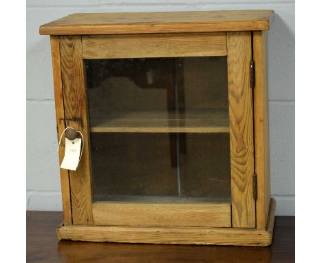 An early 20th Century pine cabinet, the rectangular top above a single glazed door enclosing a single shelf raised on a plint