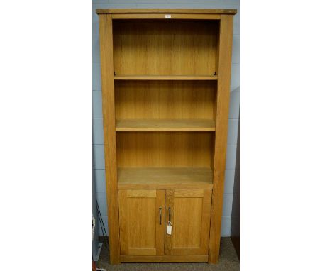 A 20th Century oak open bookcase, the projecting cornice above three open shelves and two panelled cupboard doors below enclo