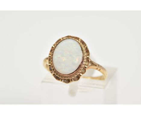 A 9CT GOLD OPAL RING, set with a central oval opal within a collet mount and scallop surround, to the bifurcated shoulders an