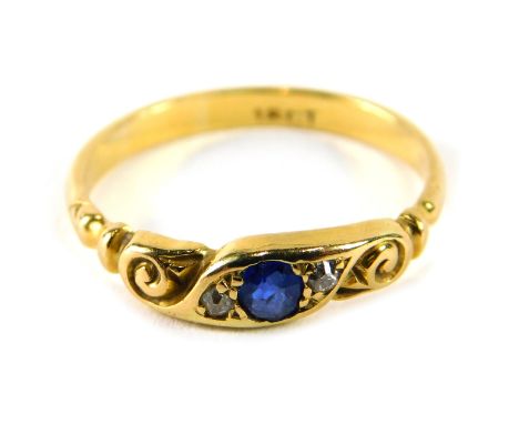 A sapphire and diamond dress ring, set with sapphire and flanked by two diamonds, with scroll sides, on a yellow metal band, 