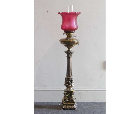 A large Victorian style brass oil lamp having a cranberry glass shade above a brass font on a fluted column supported by four