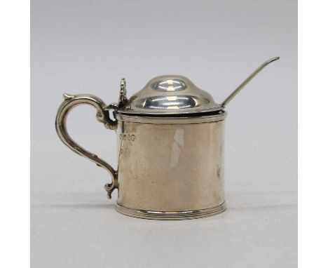 A Victorian silver mustard, of cylindrical form, having a hinged lid with shell shaped thumbpiece and scrolling handle, Londo