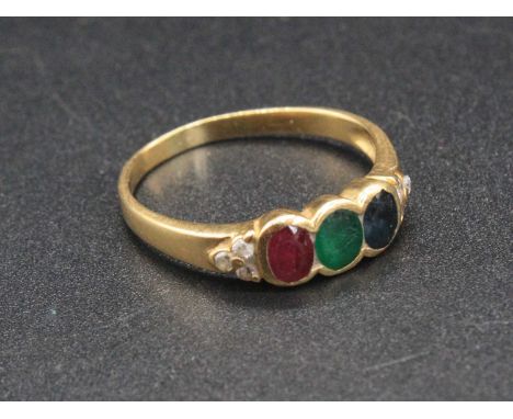 A yellow metal precious set dress ring arranged as a row of oval cut single sapphire emerald and ruby, the shoulders each set