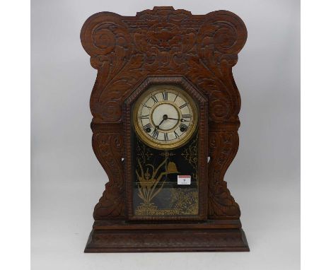 A late 19th century American walnut cased gingerbread mantel clock, having carved surround with painted dial, Roman numerals,