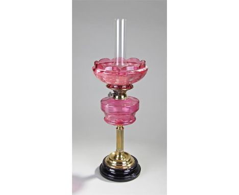 Victorian cranberry glass and brass oil lamp, the chimney above an enamel decorated shade and cranberry glass font, brass ree