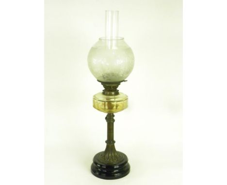 A VICTORIAN EMBOSSED BRASS OIL LAMP WITH GLASS FOUNT AND BRASS BURNER, ON BLACK GLAZED FOOT, WITH ETCHED GLASS GLOBE