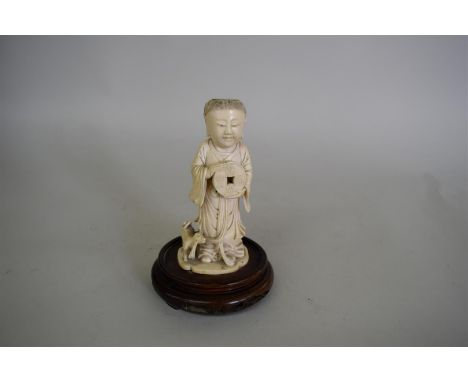 A Chinese carved ivory figure of a boy, 19th century, dressed in robes and holding an inscribed tablet or disc, with a small 