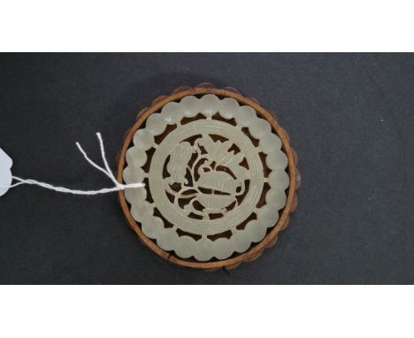 A Chinese carved and pierced celadon jade roundel, 8.2cm diameter, in wood box base of conforming form. Condition Report: No 