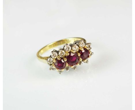 An 18ct gold ruby and diamond ring, designed as a row of three graduated round mixed cut rubies claw set in yellow gold withi