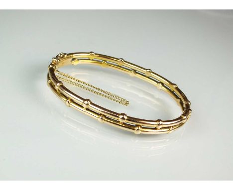 A yellow metal twin band hinged bangle, the push clasp stamped '15ct', with attached safety catch and chain, weight approx 11