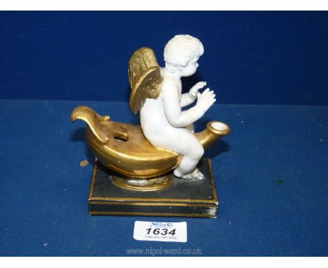 A pretty gilt finish porcelain oil lamp with a cherub sitting astride and appearing to warm his hands on the flame when lit, 