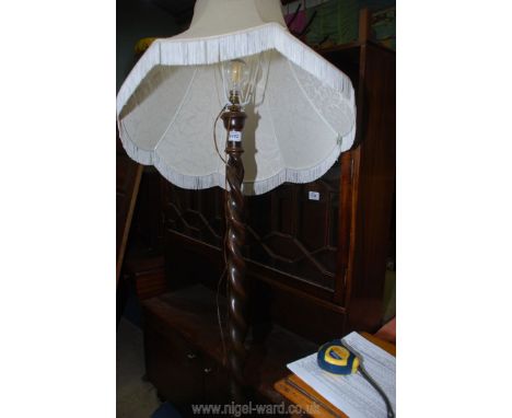 A dark Oak standard Lamp having a barley twist column, a circular base and a fringed cream eight sided fabric shade, 64'' tal