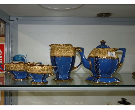 A five piece pottery tea service in blue, cream and gilt including teapot and stand, hot water jug (handle a/f.), milk jug an