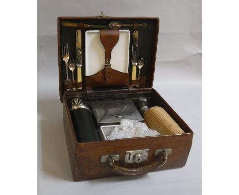 A vintage leather picnic case containing various requisites including cane covered flask, universal flask, cutlery, plates et