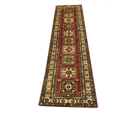 FINE KAZAK RUNNER, 255cm x 75cm, row of geometric medallions on a ruby field within complimentary bands and borders.