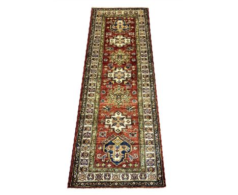 KAZAK RUNNERS, a pair, 173cm x 62cm, rows of geometric medallions on a ruby field of scattered amulates inside multiple compl