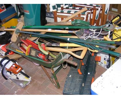 A wheelbarrow containing garden tools, trolley jack