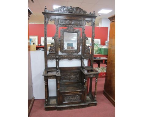 A XIX Century Carved Oak Hall Coat and Stick Stand, with scroll decorated applied top, central bevelled mirror over hinged se