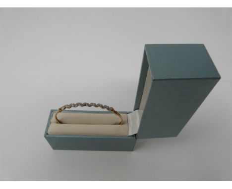 A boxed 9ct yellow and white gold diamond set bangle with hook fastening. Set with fifteen round brilliant cut diamonds in op