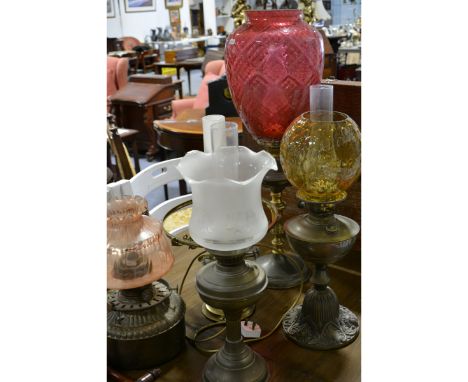 Six oil lamps, brass and chrome-plated, one having a large cranberry glass shade, all with chimneys, another lamp converted t