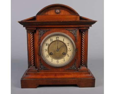 An oak cased mantle clock featuring Junghans movement, carved spiraling columns and applied metal detail37x33cm