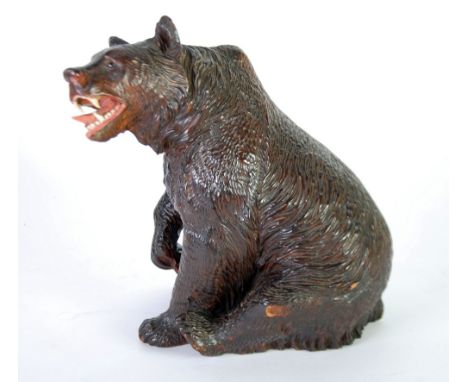 LATE NINETEENTH CENTURY BLACK FOREST CARVED WOOD BEAR, depicted in a seated post with a snarling but quizzical look, inset gl