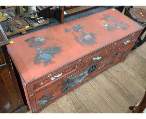 A Chinese cabinet. Decorated with motifs including precious things, on a red ground. Circa 1900. Jade handles. 50cm x 111cm x