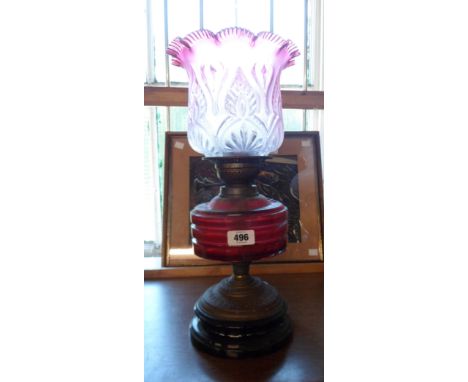 A 19th Century oil lamp with double burner, cranberry glass cut faceted reservoir, brass mounts and ceramic base and cranberr