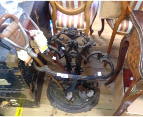 An ornate painted cast iron stick stand with pierced decoration and drip-tray, containing three shooting sticks with various 