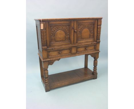 A solid, dark oak side cupboard, enclosed by a pair of carved and arcaded panel doors, two drawers beneath, front baluster-tu